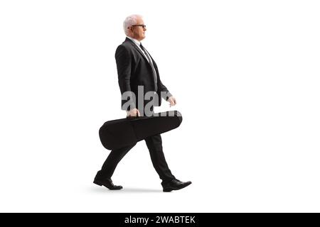 Plan de profil complet d'un homme en costume noir marchant et portant un violon dans un étui isolé sur fond blanc Banque D'Images