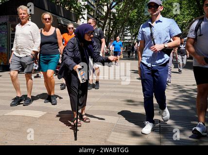 Barcelone, Espagne - 26 mai 2022 : vieille femme baissée avec un voile sombre et des lunettes à bordure de corne, appuyée sur une canne, supplie pour l'aumône dans la rue dans la fac Banque D'Images