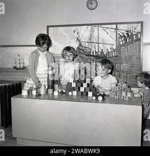 Années 1950, historique, quatre jeunes enfants dans la salle de jeux à bord d'un navire à vapeur Union Castle, avec des briques de jeu sur une table. Photo derrière eux, une peinture d'un bateau pirate. Banque D'Images