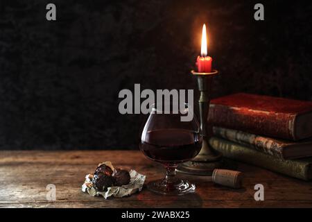 Nature morte classique avec livres vintage et bougie avec un verre de vin rouge et chocolats à fond sombre rustique (mise au point manuelle) Banque D'Images