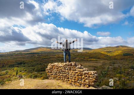 Homme debout sur un mur de forteresse en ruine, contemplant une vue imprenable sur la montagne. Contraste impressionnant entre le mur antique et la majestueuse monture Banque D'Images