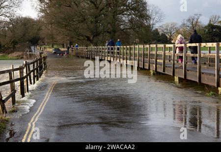 Les gens marchant sur une passerelle surélevée au-dessus de la route de l'eau qui coule en dessous après que la rivière Avon a éclaté ses rives et inondé la route à Lacock Wiltshire Banque D'Images