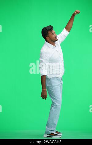 Un homme en chemise blanche, sur fond vert, en pleine hauteur, leva la main, de profil Banque D'Images