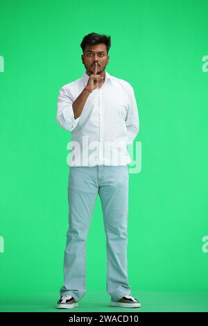 Un homme en chemise blanche, sur fond vert, en pleine hauteur, montre un signe de silence Banque D'Images