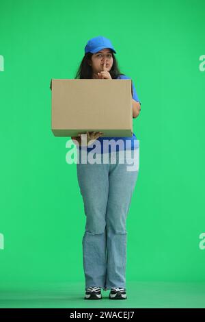 Une femme accoucheuse avec une boîte, sur fond vert, en pleine hauteur, montre un signe de silence Banque D'Images