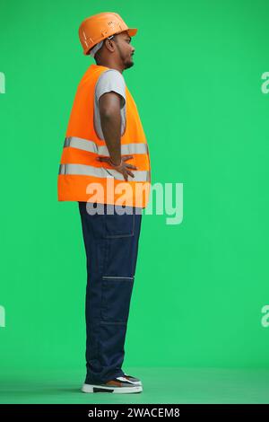 Un ouvrier du bâtiment, sur un fond vert, tient ses mains sur sa ceinture, de profil Banque D'Images