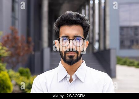Portrait d'un jeune homme d'affaires proche, à l'extérieur de l'immeuble de bureaux, un homme regarde avec confiance dans la caméra, un travailleur dans la chemise réfléchit et se concentre. Banque D'Images