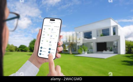 Femme contrôle la température et les appareils domestiques avec une application de maison intelligente. Maison moderne et écologique avec cour verte en arrière-plan Banque D'Images
