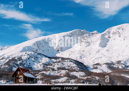 Chalet en bois isolé dans un petit village enneigé au pied des montagnes Banque D'Images