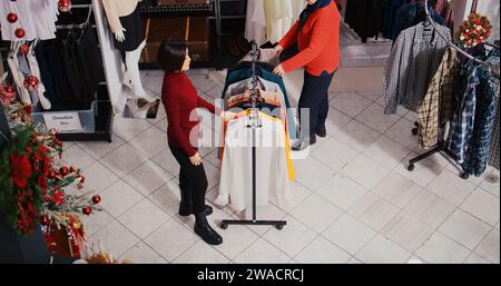 Homme afro-américain habillé en Père Noël dans le magasin de vêtements de centre commercial sur le thème de Noël. L'employé jaillit des cloches de Noël et tient le paquet rouge présent dans la boutique décorée festive Banque D'Images