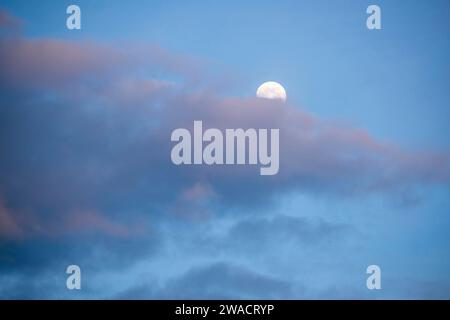 La pleine lune se lève derrière des nuages colorés à Woodland, CA, USA en décembre 2023. Banque D'Images