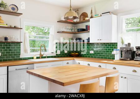 Un détail de cuisine avec des comptoirs en bois de bloc de boucher, des armoires blanches, un luminaire en or suspendu au-dessus de l'île et un dosseret de tuile de métro vert. Banque D'Images