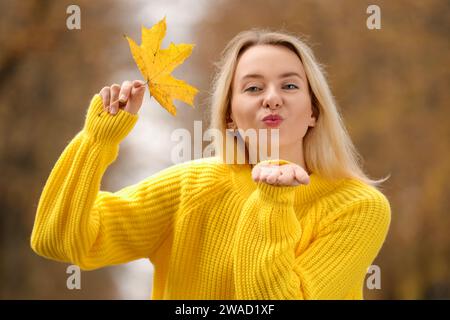 Belle femme avec feuille d'automne soufflant baiser à l'extérieur Banque D'Images