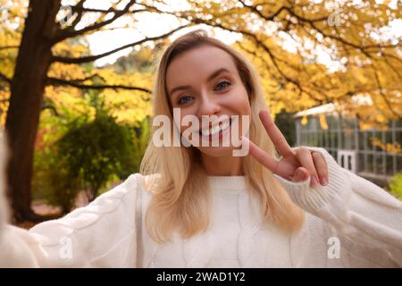 Portrait de femme heureuse prenant selfie et montrant signe de paix dans le parc d'automne Banque D'Images