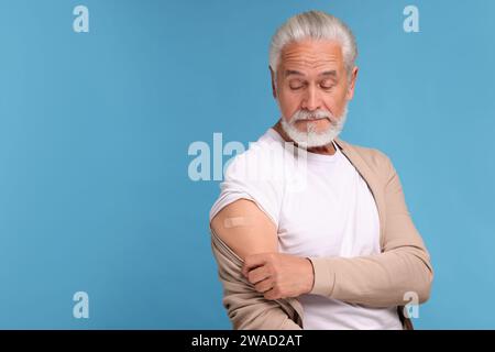 Homme âgé avec un bandage adhésif sur le bras après la vaccination sur fond bleu clair, espace pour le texte Banque D'Images