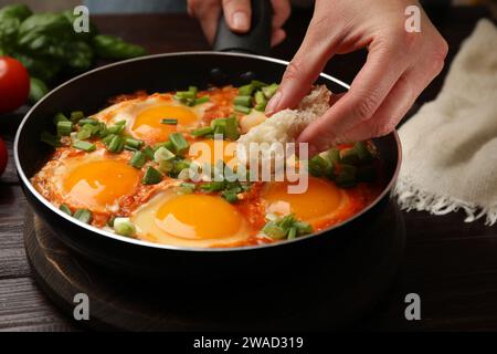 Femme trempant morceau de pain dans délicieux Shakshuka à la table en bois, closeup Banque D'Images