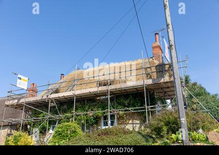 Cottage anglais dans le Dorset avec échafaudage érigé pour entreprendre des réparations et l'entretien de toit de chaume, Angleterre, Royaume-Uni, 2023 Banque D'Images