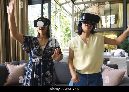 Heureuses amies asiatiques jouant et utilisant des casques vr à la maison. Vie domestique, technologie, amitié et mode de vie, inchangés. Banque D'Images