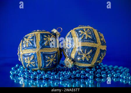 Une paire de boules arbre de Noël bleu et or, photographiées avec un collier de perles bleues, sur un fond bleu Banque D'Images