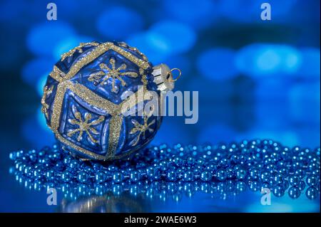 Une boule arbre de Noël bleue et or, photographiée avec un collier de perles bleues, sur fond bleu Banque D'Images