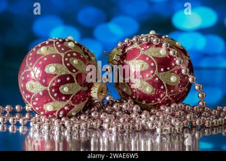 Une paire de boules sapin de Noël rouge et or, photographiées avec un collier de perles blanches, sur fond bleu Banque D'Images