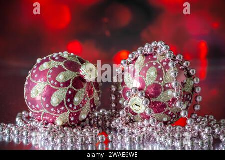 Une paire de boules sapin de Noël rouge et or, photographiées avec un collier de perles blanches, sur fond rouge Banque D'Images