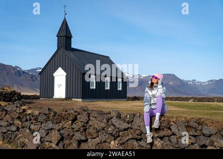 Une jeune femme portant un imperméable jaune vif pose sur un mur de pierre devant une église rurale Banque D'Images