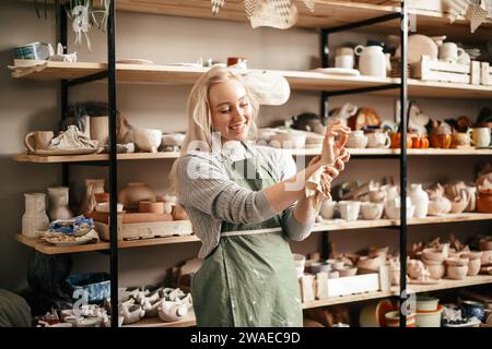 Souriant potier féminin dans l'atelier contre rack de poterie Banque D'Images