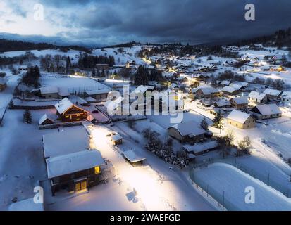 Vue sur la chaîne de montagnes enneigées et le village avec des maisons illuminées situées au bas de la colline en Slovaquie au coucher du soleil Banque D'Images