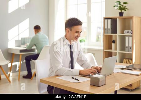 Portrait de jeune homme d'affaires attrayant travaillant sur un ordinateur portable au bureau Banque D'Images