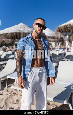 Un jeune homme tatoué posant sur une plage Banque D'Images