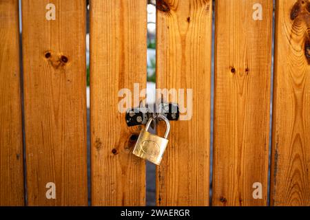 Portail en bois du jardin de la maison. La porte est fermée avec un cadenas. Cadenas en métal sécurisant un portail en bois. Casier sur porte en bois. Personne, photo de rue Banque D'Images