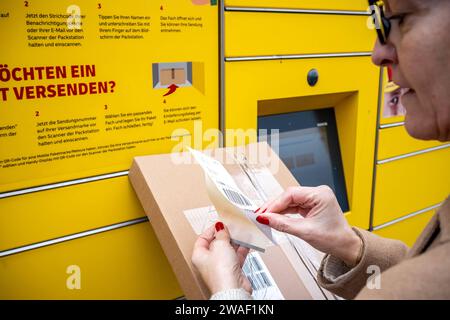 Innovative Paketlogistik - Nutzung der DHL Packstation 04.01.2024, Bad Camberg : Symbolfoto, Illustrationsbild, Symbolbild, Illustrationsfoto Das Bild zeigt eine Frau im Anschnitt, die mit ihrem smartphone über den Touchscreen einer DHL Paketstation interagiert, UM ein Paket einzureichen. SIE ist konzentriert auf die digitale Schnittstelle fokussiert, während ihre hand das Mobiltelefon hält und die entsprechenden Eingaben auf dem Bildschirm der Paketstation tätigt UM das Paket einzulegen. Die Packstation, ein Paketautomatensystem von DHL, bietet seit 2001 in über 12,500 Standorten deutschlandwe Banque D'Images