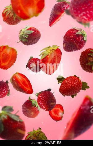 Fraises et fraises tranchées volant dans l'air, isolé sur fond rose. Banque D'Images