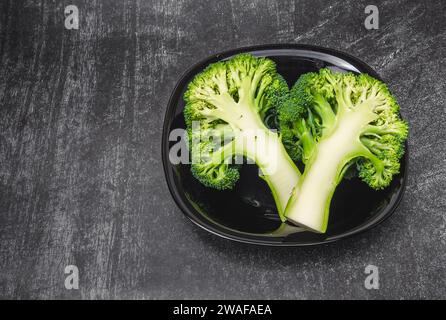 Deux moitiés de brocoli vert frais dans un bol noir sur fond gris. Une alimentation saine. Banque D'Images