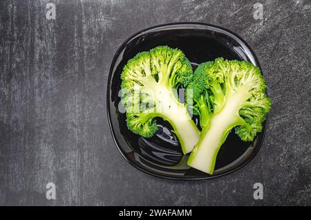 Deux moitiés de brocoli vert frais dans un bol noir sur fond gris. Une alimentation saine. Banque D'Images