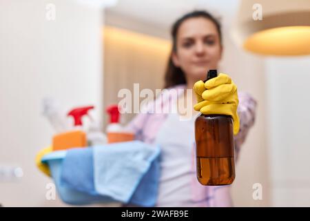 Femme dans les gants de protection jaune en caoutchouc pulvérisant du détergent et tenant le seau avec des outils de nettoyage. tâches ménagères. espace de copie Banque D'Images
