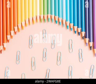 Crayons arc-en-ciel colorés se trouvent dans une rangée avec des trombones sur un fond beige Banque D'Images