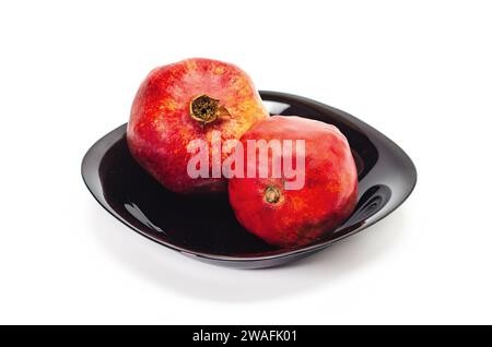 Deux grenades rouges mûres dans un bol noir isolé sur un fond blanc. Fruits juteux. Banque D'Images