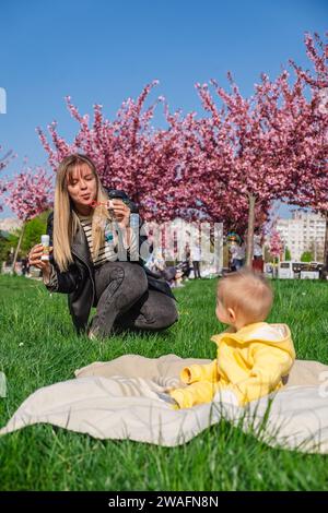 Joyeux mère et fils jouent avec des bulles près des fleurs de cerisier Banque D'Images