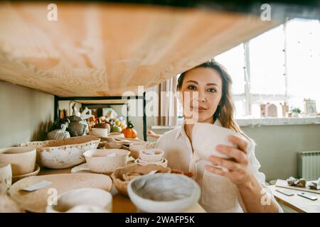 Jeune femme gestionnaire de l'atelier de poterie arrange les produits sur l'étagère Banque D'Images