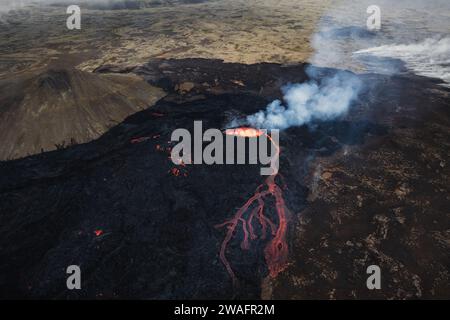 Éruption volcanique en Islande, cratère sommital, expulsion de gaz, et lave fondue se déversant d'un évent, vue latérale aérienne. Risques naturels et géothermie Banque D'Images