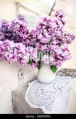 Bouquet de lilas violet dans un vase en céramique blanche sur serviette tissée près du miroir vintage décor d'intérieur avec des fleurs fraîches. Banque D'Images