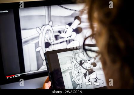 Une femme regarde le dessin animé « Steamboat Willie » de Walt Disney Co. À New York le mardi 2 janvier 2024. Steamboat Willie, la version originale de l'emblématique Mickey Mouse est entrée dans le domaine public avec l'expiration cette année de sa protection des droits d'auteur. (© Richard B. Levine) Banque D'Images