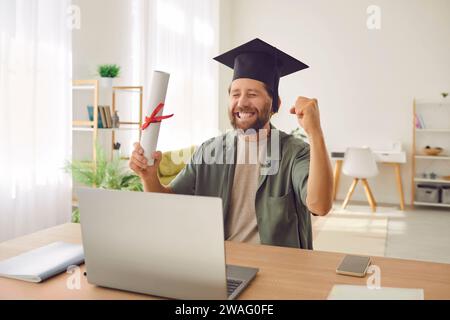 Homme diplômé assis au bureau avec diplôme faisant le geste oui pendant l'appel vidéo en ligne. Banque D'Images