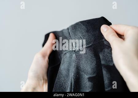 La main d'une femme montre des marques blanches sur des taches de déodorant sur des vêtements noirs. Vêtements abîmés. concept de coloration de la vie quotidienne. Banque D'Images