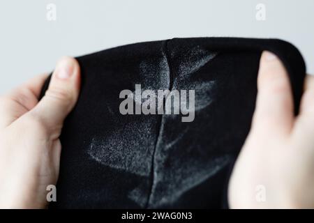 La main d'une femme montre des marques blanches sur des taches de déodorant sur des vêtements noirs. Vêtements abîmés. concept de coloration de la vie quotidienne. Banque D'Images