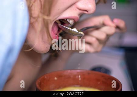 fille mange de la soupe chaude avec une cuillère d'une assiette d'argile Banque D'Images