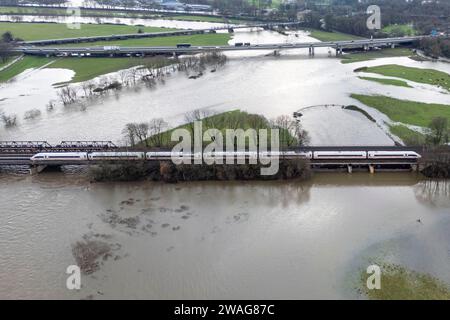 04 janvier 2024, Rhénanie du Nord-Westphalie, Mülheim an der Ruhr : un train DE GLACE traverse un pont dans les prairies de la Ruhr, qui sont inondées par les hautes eaux. (Vue aérienne avec un drone) photo : Christoph Reichwein/dpa Banque D'Images