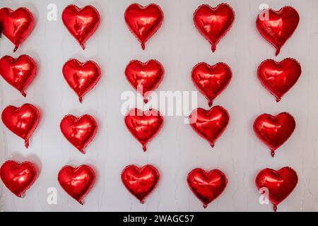 Sur un mur blanc à l'intérieur, il y a des ballons rouges en aluminium en forme de cœur. Décor, décoration de la maison pour la Saint Valentin. Dos lumineux et créatif Banque D'Images